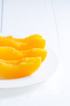 Slices canned peach on white wooden table