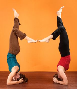 Two women in a coordinated yoga posture over orange background
