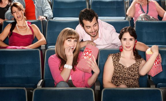 Smiling ladies sharing popcorn with man in theater
