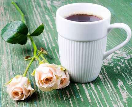 Сup of coffee with sprig roses on old wooden table