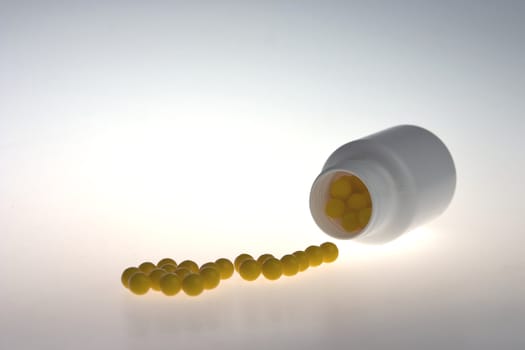 varicoloured pills of vitamins, poured out from a vial on a white background