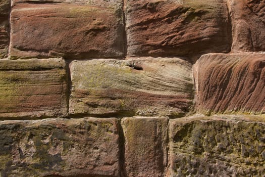 A wall constructed of red, cut sandstone with curves and textures held together with cement pointing.
