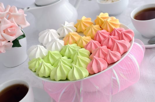 Meringue cookies of different colors on a plate with a cup of coffee