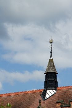 A turet on a red tile roof made from wood and slate with an ornate lightening rod with a crown as a symbol.