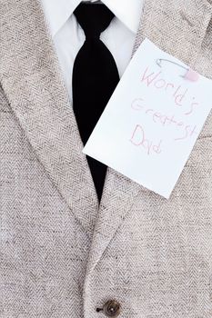 Man's suit jacket, tie and shirt with World's Greatest Dad note pinned over his heart.
