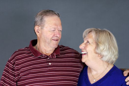 Happy senior couple laughing together, studio shot over grey background.