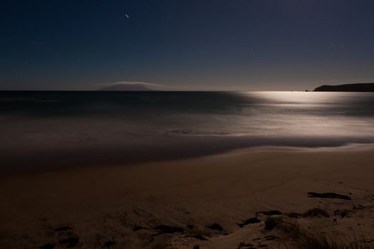 Long exposure shot of romantic sand beach lit by the moon, the light of which being reflected on ocean surface