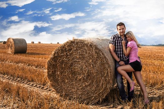 Loving attractive young couple standing in a close embrace in an agricultural field alongside a circular hay bale