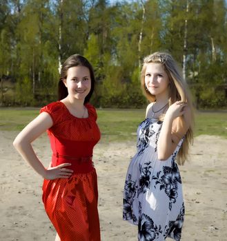 Two girls in dresses walk in the park on a sunny day