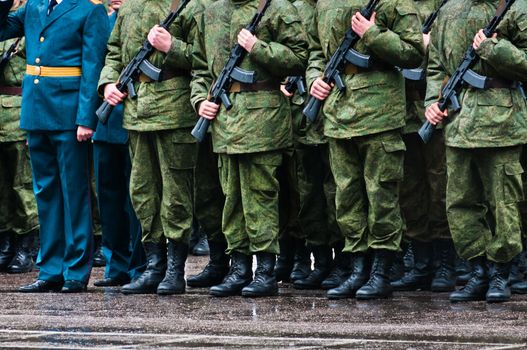 Soldiers in camouflage stand in formation with officer in blue clothing