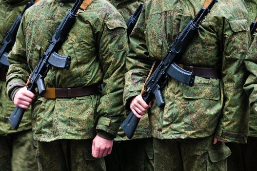 Soldiers in camouflage stand in formation with weapons body only