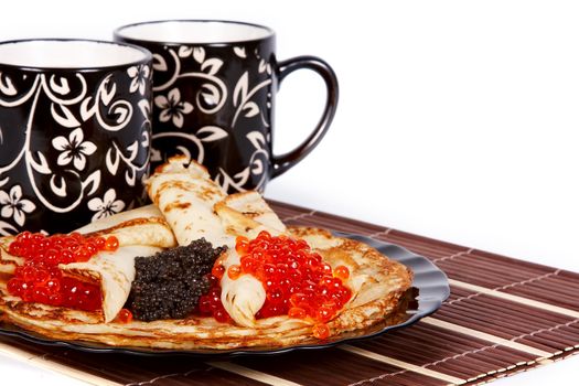 Cups with tea and a pile of pancakes with caviar on a plate