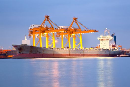 Big Container Cargo freight ship with working crane in shipyard at dusk for Logistic Import Export background