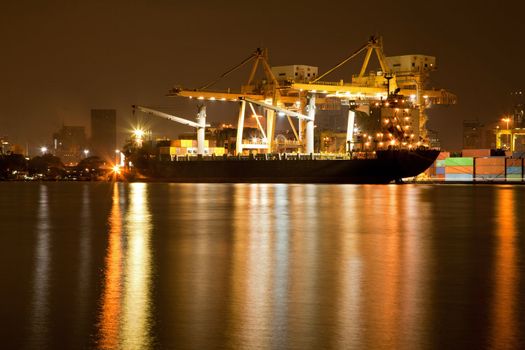 Big Container Cargo freight ship with working crane in shipyard at night for Logistic Import Export background