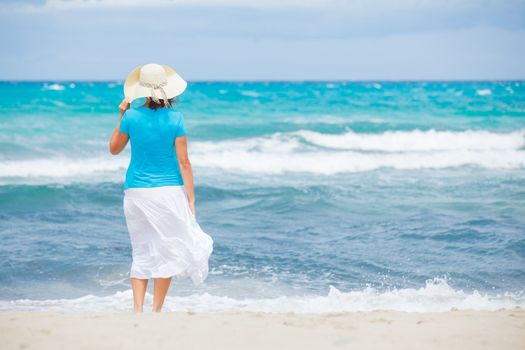 Happy beautiful woman in the beach hat looking at the sea