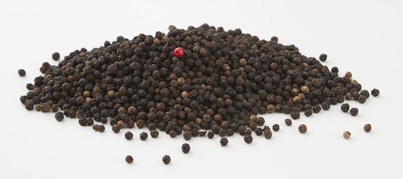 pile of ungrounded black pepper, with one acorn of red pepper