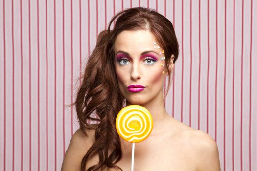 Young woman with colorful makeup and star candy glued to her face, holding an orange lollipop