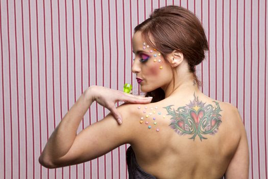 Young woman with colorful makeup and star candy glued to her face and body, blowing on a lollipop ring