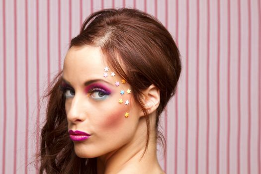 Young woman with colorful makeup and star candy glued to her face 