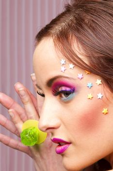 Young woman with colorful makeup and star candy glued to her face, showing a lollipop ring