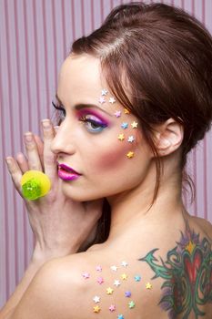 Young woman with colorful makeup and star candy glued to her face, showing a lollipop ring