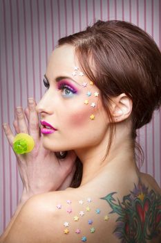 Young woman with colorful makeup and star candy glued to her face and a lollipop ring
