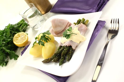 green Asparagus with hollandaise sauce, potatoes and delicious cooked ham on a bright background