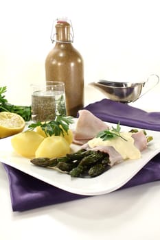 fresh Asparagus with hollandaise sauce, potatoes and cooked ham on a bright background