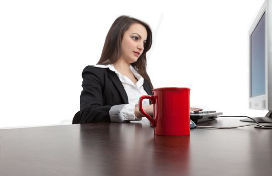 Image of a young woman working on a computer with a red cup of coffee on her desk.Selective focus on the red cup.
