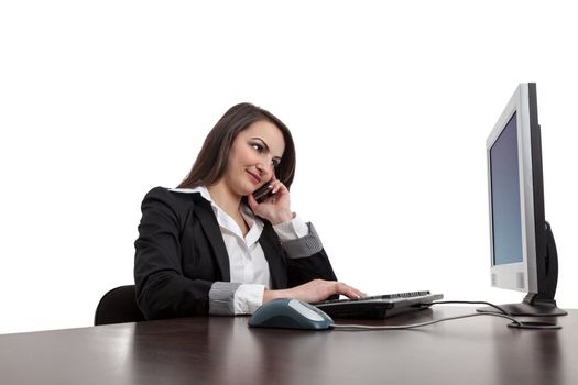 Image of a young brunette woman working on a computer and using a mobile phone , isolated against a white background.