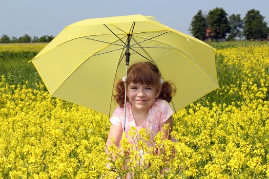 beautiful little girl with umbrella standing in yellow flowers field