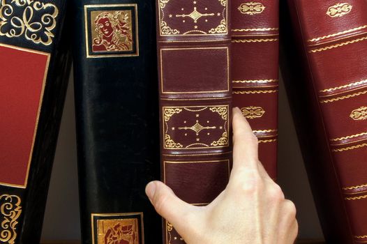 A row of antique books with a human hand holding one