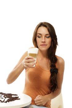 beautiful woman sitting on a table looking at the latte macchiato coffee in her hand on white background