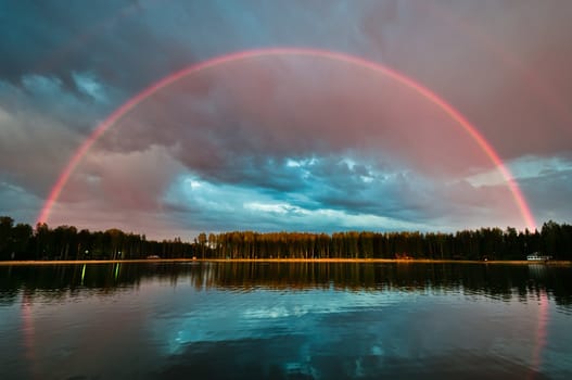 Full beautiful rainbow arc over the lake with still water