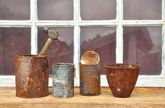 Rusty old tin cans used for tools in front of an old window.