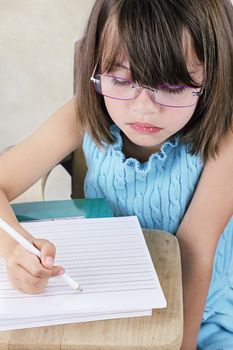 Little girl sitting at a school desk writing.