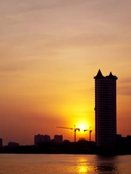 Buildings with construction site and river silhouette in the orange sunset