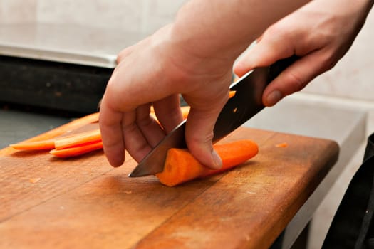 The cook cut carrots on a cutting Board.