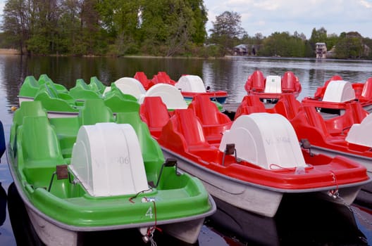 Water bicycles green and red locked at lake pier. Two-man active recreation vehicle equipment objects.
