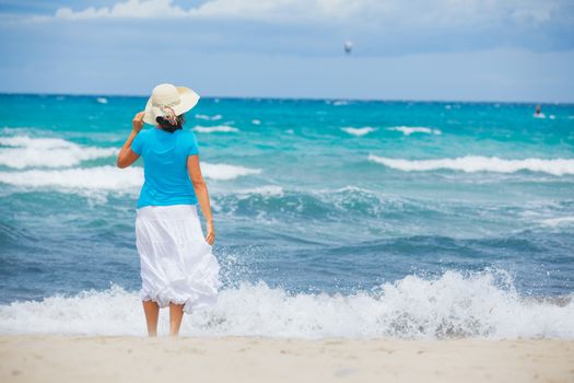 Happy beautiful woman in the beach hat looking at the sea