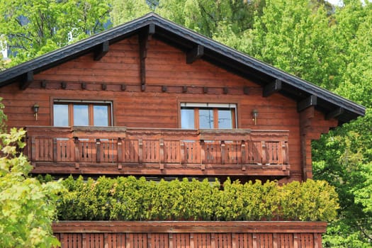 Close up of a brown wooden chalet among green leaves of summer trees, Crans Montana, Switzerland