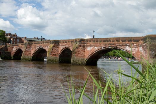 An historic red sandstone bridge with arches and a flowing river against a sky with cloud.