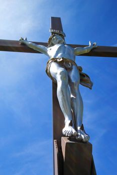 White sculpture of Jesus on a wood cross and sunny blue sky