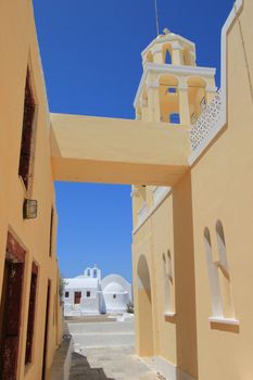 Side of blue yellow wall and arch of a greek orthodox church and small white chapel far on the photo in Santorini island, Greece, by beautiful weather