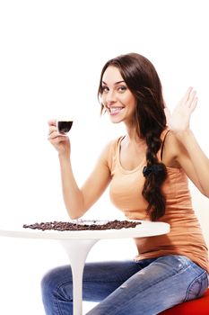 happy young woman sitting at a table holding cup of espresso coffee on white background