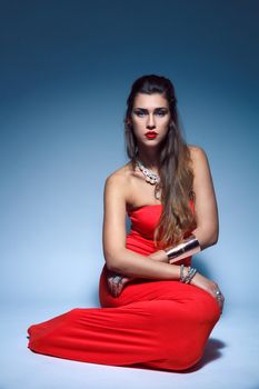 Beautiful fashion young woman in a red dress sitting in the studio