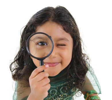 A little Indian girl peers at the camera through a magnifying glass, isolated on white background