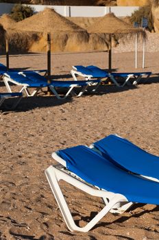 blue chairs at a beach (intentional defocused background with more chairs and umbrellas made with coconut leaves), picture taken in Albufeira (Algarve), Portugal