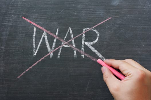 War - word crossed out with red chalk on a smudged blackboard, with a hand holding red chalk