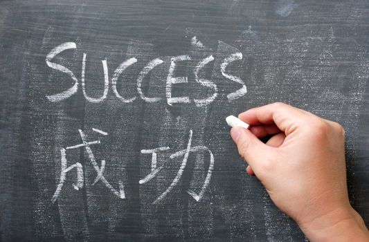 Success - word written with chalk on a blackboard with a Chinese translation, with a hand holding chalk